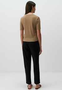 Tan geribbelde top met korte mouwen en een ronde halslijn, gedragen met zwarte rechte broek. De stof heeft een zachte textuur en een licht gesculpteerde zoom.