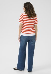 Haut à manches courtes rayé rouge et blanc associé à un jean en denim bleu à jambes larges. Les jeans comportent des poches arrière et une finition soignée.