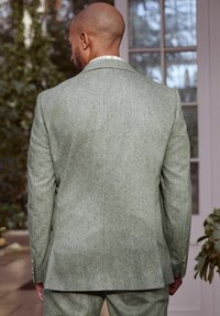 Skræddersyet grøn jakkesæt lavet af tekstureret stof, med en enkelt slids, notch-krave og knapmanchetter. Bagview med et elegant, minimalistisk design.