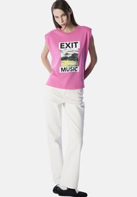 Roze katoenen t-shirt met brede schouders, voorzien van een grafische print van abstracte kunst en de tekst "EXIT MUSIC," gecombineerd met witte broek.