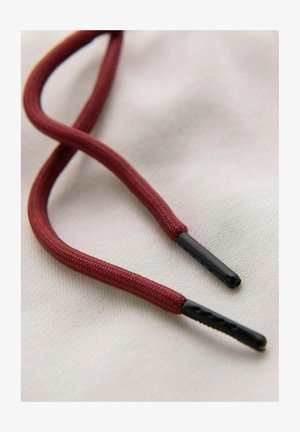 Gros plan d'un lacet rouge avec des embouts en plastique noir sur un fond en tissu blanc texturé.