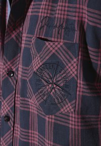 Karierte Hemd in Marineblau und Rot, aus Baumwollmaterial, mit einer Brusttasche mit gesticktem Kompassdesign und Knopfverschluss.