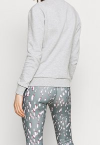 Sweatshirt gris avec des poignets et un ourlet côtelés, assorti à des leggings ajustés présentant un fond vert et des motifs abstraits blancs et roses.