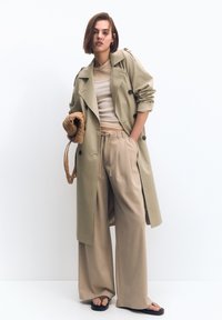 Palton bej cu nasturi dublu rând, asortat cu un top crem ajustat și pantaloni bej cu picioare largi. Accesoriu: geantă împletită maro.