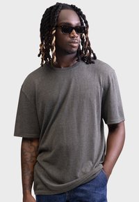 Gray short-sleeve T-shirt in soft fabric with a relaxed fit and round neckline. Worn with blue jeans and sunglasses.