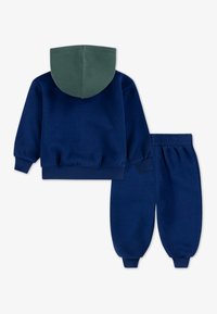 Felpa navy con cappuccio verde, dotata di maniche lunghe e polsini a coste. Pantaloni della tuta navy abbinati con vita elastica e gambe tapered.