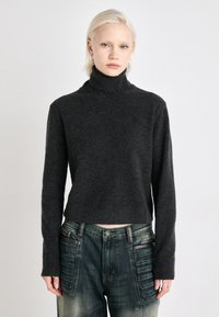 Suéter de gola alta cinza escuro, feito de um tecido macio, com mangas compridas e um design cropped, combinado com jeans de denim desbotados com detalhes texturizados.