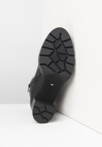 Semelle de botte noire avec un motif de relief géométrique reposant contre un mur blanc, affichant "NeroGiardini Fabriqué en Italie" estampé.