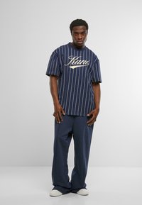 Jūras spēku joslu īsām piedurknēm krekls ar tekstu "Stay", apvienots ar brīvām jūras spēku biksēm un baltām kurpēm, veidojot ikdienišķu apģērbu.