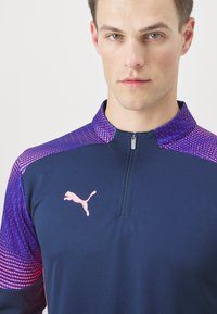 Marineblaue sportliche Quarter-Zip-Shirt mit lila Farbverlauf-Details und strukturierter Stoffqualität; beinhaltet ein pinkes Puma-Logo auf der Brust.