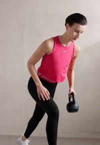 Ružičasti bezrukavni atletski top s bijelim natpisom "PRO", uparen s crnim tajicama. Osoba drži crni kettlebell, prikazujući poziciju tijekom vježbanja.