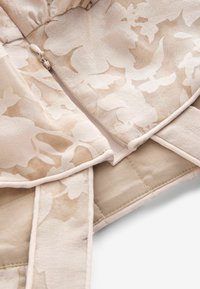 Beige floral-patterned fabric with a smooth texture, featuring a discreet zipper and solid beige lining. Accented with light piping.