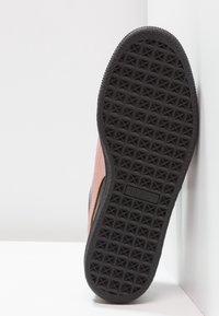 Černá gumová podrážka s texturovaným gripem a viditelným logem Puma, růžová vrchní část částečně zobrazená na bílém pozadí. 