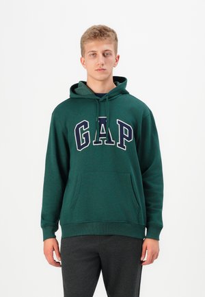 Grønn fleece hettegenser med kengurulomme, med store hvite og marineblå "GAP" bokstaver på forsiden. Ledig passform, ribbestrikkede mansjetter.