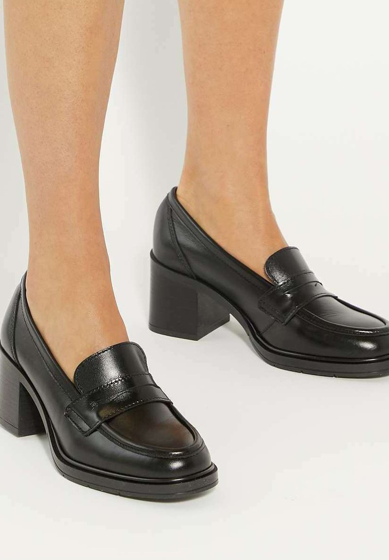 Black leather heeled loafers with a smooth finish, featuring a rounded toe and a block heel. Accents include a raised seam and band detail.