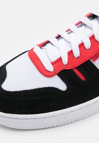 Svart, vit och röd sneakers med en mesh-överdel, mockadetaljer, platta snören och en strukturerad gummisula med varumärke.