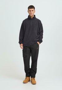 Tumehallast poollukuga fliispulloverit, millele on kombineeritud musta värvi lahtiste küljetaskutega töörõivad ja kollakaspruunide paeltega saapad.