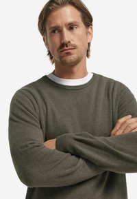 Mörkgrön tröja med rund halsringning och långa ärmar, tillverkad av mjukt tyg. Designen har en enkel, ren siluett.