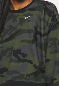 Sweat-shirt camouflage vert et noir avec un col rond, arborant un logo Nike blanc sur la poitrine et un tissu texturé.