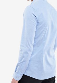 Lichtblauw overhemd met lange mouwen en een button-down kraag, gladde textuur en manchetten met één knop, met een detail van de achterste yoke.