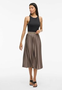 Un haut sans manches noir associé à une jupe plissée mi-longue taupe et des sandales noires. Tissu lisse avec un doux éclat et une taille élastique.