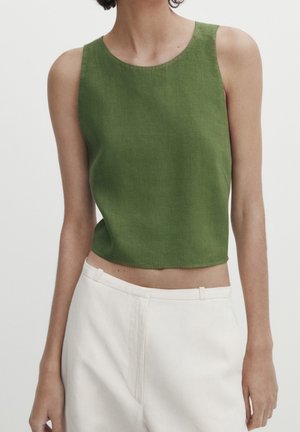 Zielony lniany krótki top z okrągłym dekoltem i bez rękawów, zestawiony z jasnobeżowymi, dopasowanymi spodniami. Gładka faktura i czyste linie.