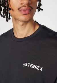 Svart bomull t-skjorte med rund hals og hvit "TERREX" logo på øvre venstre side. Glatt tekstur, uformell design.