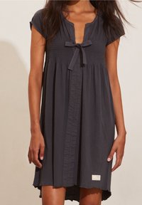 Tmavě šedé šaty s krátkými kápovými rukávy, řaseným poprsím, výstřihem do V, předním zapínáním na knoflíky a asymetrickým lemem. Obsahují dekorační mašli.