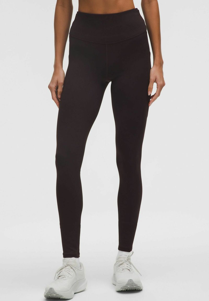 Leggings negre cu talie înaltă, realizate dintr-un material elastic, având o textură netedă și un design aderent. Asortate cu pantofi sport albi.