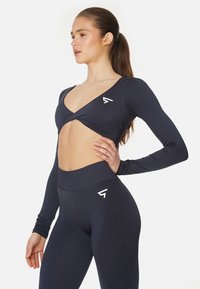 Navy Langarm-Crop-Top mit tiefem V-Ausschnitt und Cut-Out-Design, kombiniert mit hochgezogenen Leggings, die ein dezentes Texturmuster aufweisen.