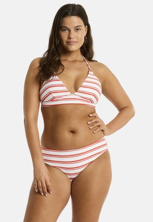 Kobieta o długich ciemnych włosach, ubrana w biały bikini w poziome czerwone paski, stojąca z jedną ręką na biodrze na białym tle.