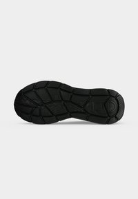 Semelle de chaussure en caoutchouc noire avec des motifs de grip texturés, comprenant des lignes angulaires et courbes, présentée sur un fond clair uni.