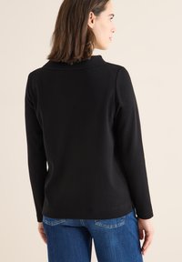 Black long-sleeve top made of soft material, featuring a classic collar and a straight cut, paired with blue denim jeans.