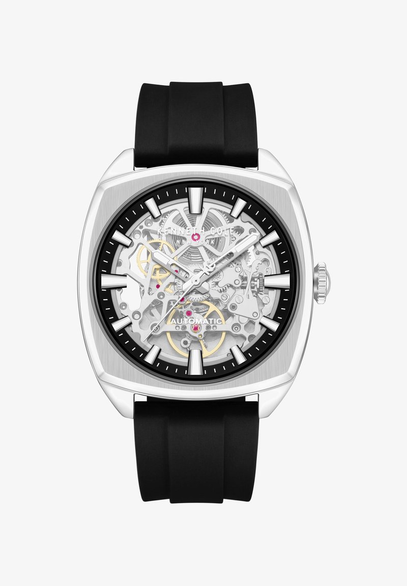 Montre automatique Kenneth Cole avec bracelet en silicone noir, boîtier carré argenté et cadran squelette visible montrant les engrenages et les marqueurs.