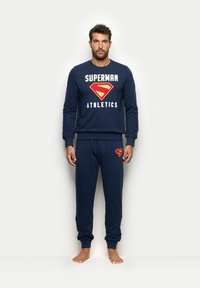 Granatowy zestaw składający się z bluzy i spodni z napisem "SUPERMAN ATHLETICS". Posiada żółte i czerwone logo Supermana. Wykonany z mieszanki bawełny, o luźnym kroju.