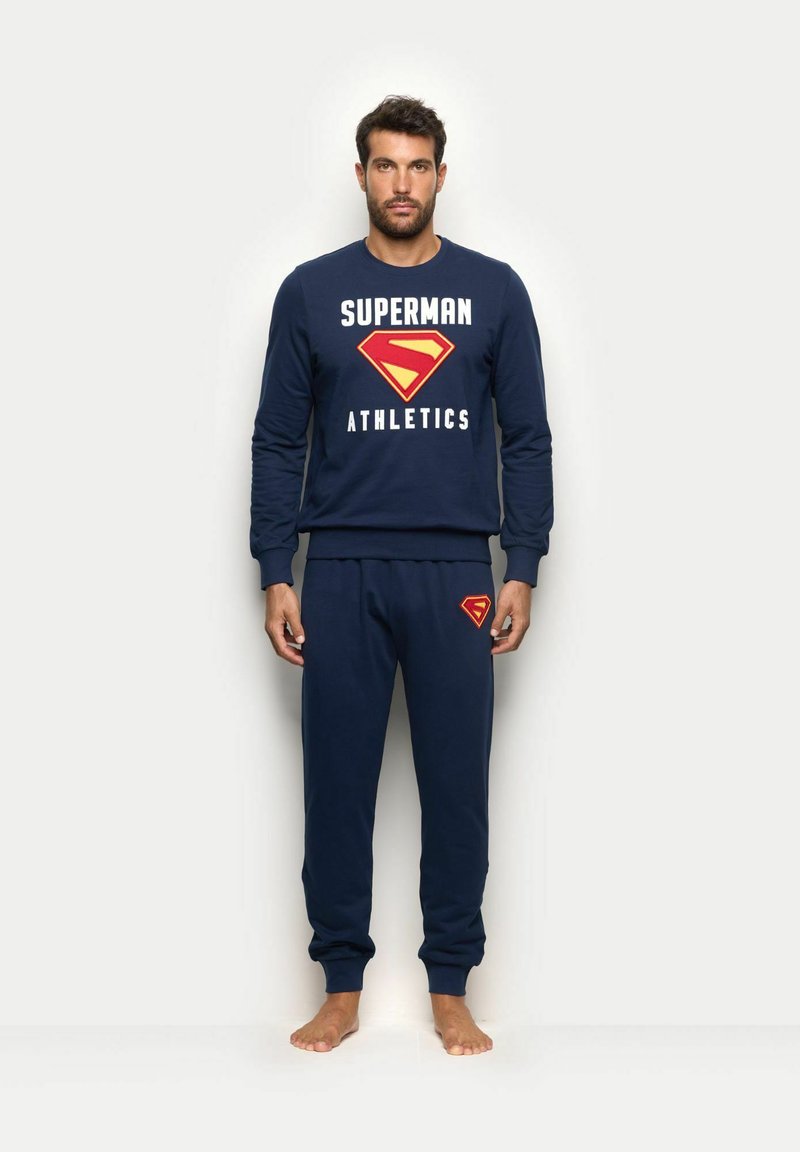 Granatowy zestaw składający się z bluzy i spodni z napisem "SUPERMAN ATHLETICS". Posiada żółte i czerwone logo Supermana. Wykonany z mieszanki bawełny, o luźnym kroju.