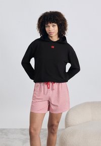 Fekete kapucnis pulóver vörös logóval, piros mintás nadrággal párosítva. Az anyagok simák, és a nadrág elasztikus derékrésszel rendelkezik.