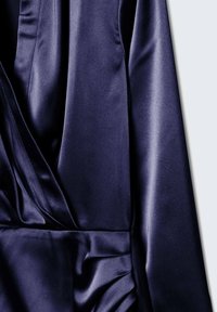 Detail námořnického saténového šatu se skládá z draped designu s jemnou texturou, decentním leskem a nabíraným švem na boční straně.