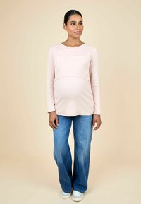 Pikkade varrukatega hele roosa rasedustopp, millel on soonikuline tekstuur, koos helehallide laia lõikega teksade ja valgete tossudega neutraalses taustas.