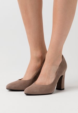 Talons hauts en suede marron avec un bout rond, présentant une texture lisse et un talon épais, placés sur un fond uni.