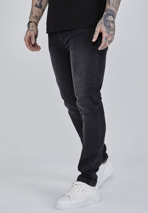 Black slim-fit jeans with a smooth texture, featuring subtle fading details. Paired with white sneakers, highlighting a clean silhouette.