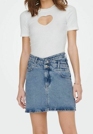 Kobieta ubrana w biały top z krótkim rękawem i wycięciem w kształcie serca oraz niebieską spódnicę jeansową z wysokim stanem i podwójnym zapięciem na guziki.