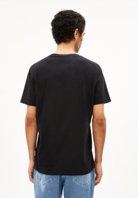 Schwarzes Baumwoll-T-Shirt mit kurzen Ärmeln und Rundhalsausschnitt, hat einen geraden Schnitt und wird mit blauen Jeans kombiniert.