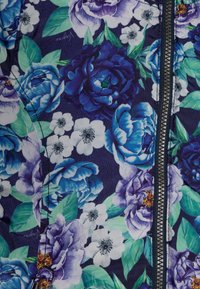 Tessuto floreale con grandi peonie viola e blu, accompagnate da foglie verdi su uno sfondo blu scuro. Include un dettaglio della cerniera in contrasto.