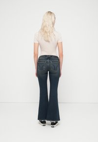 Σκούρα μπλε τζιν με καμπάνα, στενή μέση και διακοσμητική ραφή στις πίσω τσέπες. Συνδυασμένα με εφαρμοστό ανοιχτόχρωμο τοπ και αθλητικά παπούτσια.