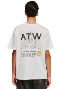 Hvid bomulds t-shirt med grafisk design af bjerge og teksten "ATW" i grøn. Inkluderer branding og plejeetiketdetaljer nederst.
