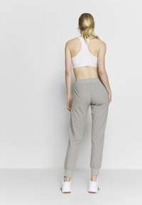 Gray sweatpants with elastic cuffs and a drawstring waistband, paired with a white sports bra. Model seen from the back, wearing white sneakers.