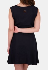 Abito a maniche corte di un blu navy scuro con gonna svasata. Presenta un collo rotondo e un piccolo logo arancione sulla schiena. Tessuto morbido.