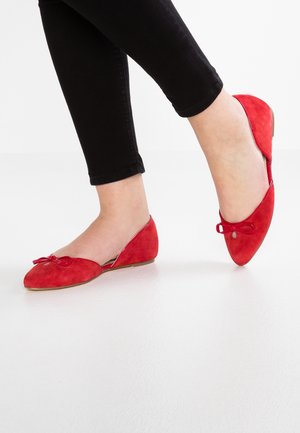 Červené semišové baletní byty s kulatou špičkou, zdobené malou mašlí a nízkým podpatkem. Nosené s černými zkrácenými džíny.