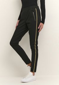 Pantalons noirs avec un design fuselé, featuring une bande dorée sur le côté et une poche zippée. Fabriqués dans un matériau extensible.